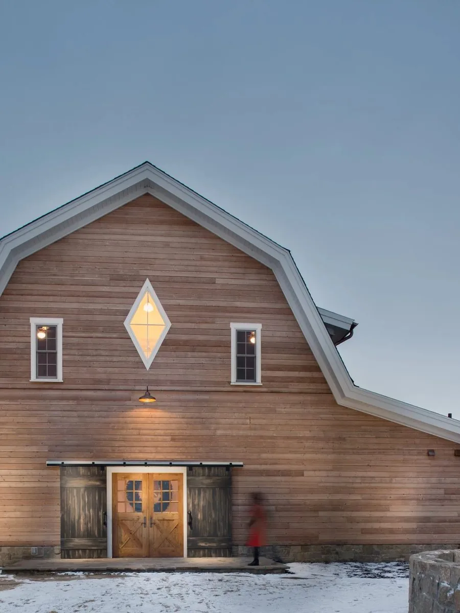 A timber and board barn-form home standing in snow at dusk
