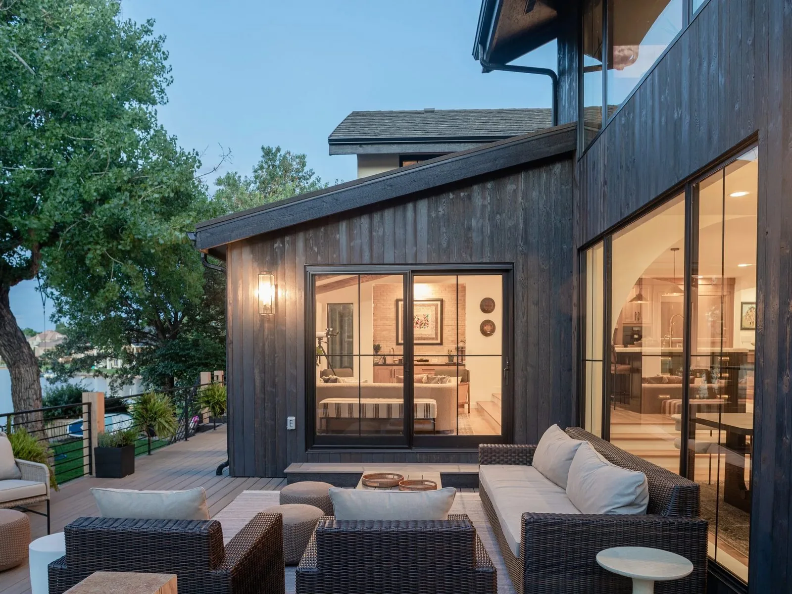 A covered deck with lounge seating beside dark stained siding and large sliding glass doors