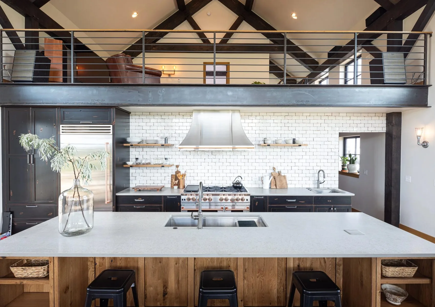 A kitchen with dark cabinetry, open shelving and a loft walkway above
