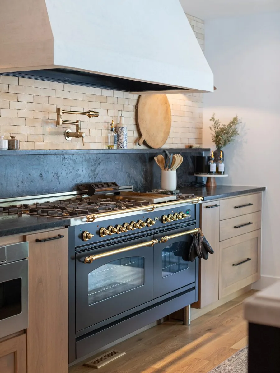A range and hood set into a stone and tile backsplash with brass fittings