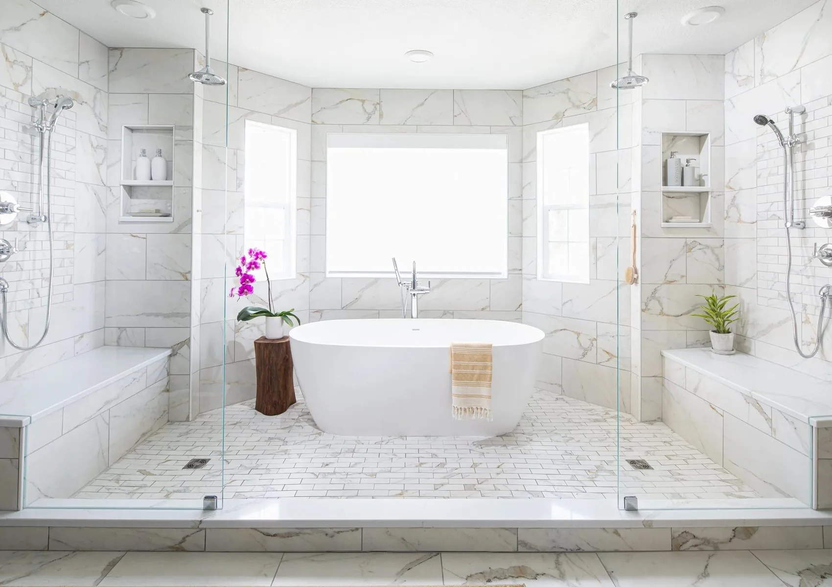 A primary bathroom in marble with a freestanding tub between two showers