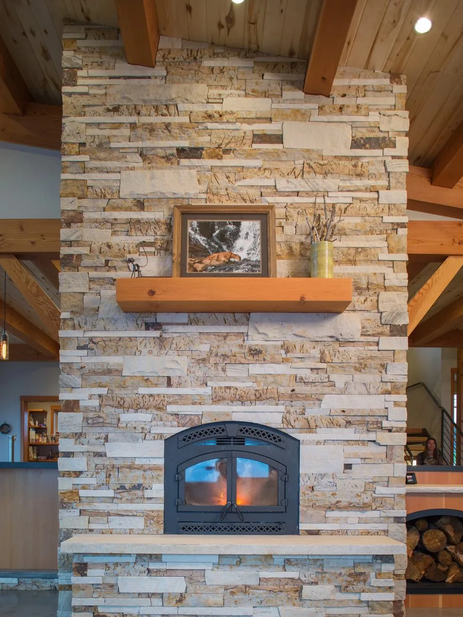A stacked stone fireplace with a timber mantel and a stack of split wood